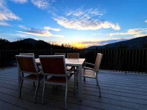 set of 6 chairs around a table set up on the deck with a dramatic golden sunset in the background