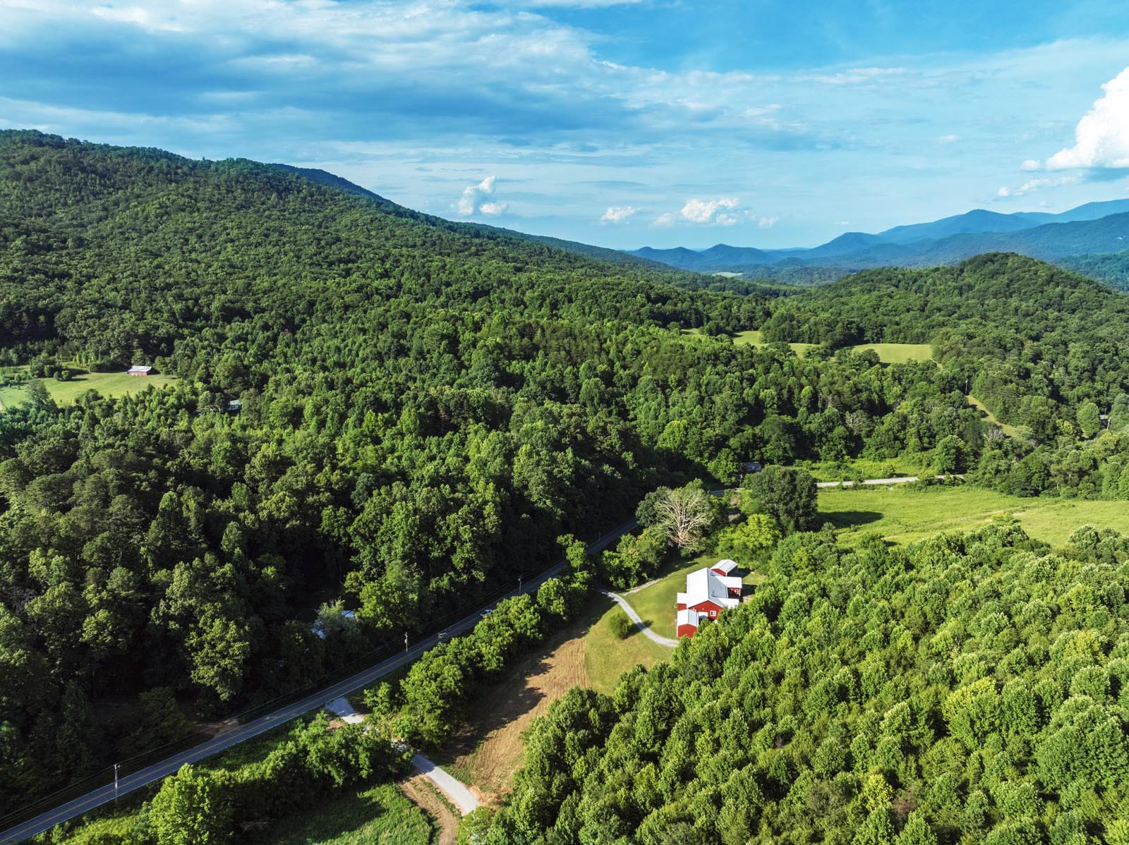 blue ridge mountain ranges in the distance with a red modern farmhouse surrounded by green trees