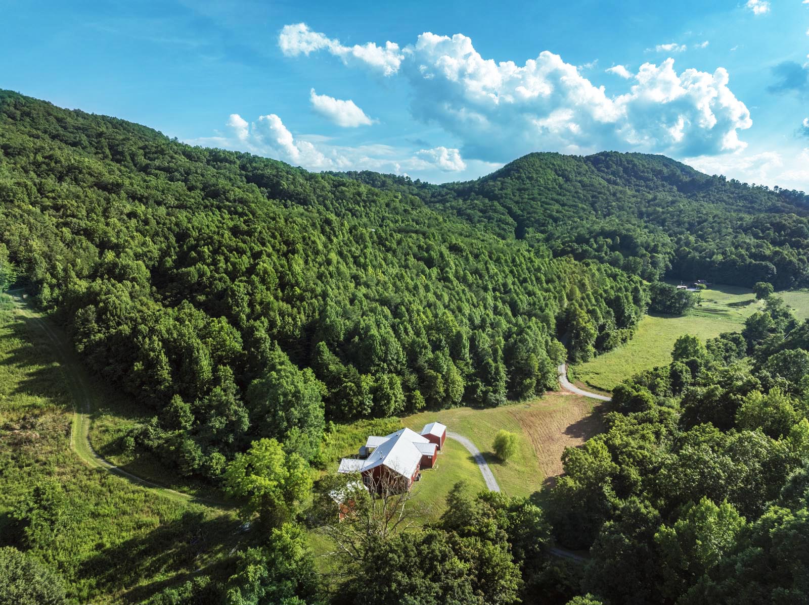 a red modern farmhouse with a white roof looks very small surrounded by mountains covered with a lush forest