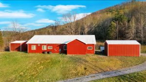 photo of backside of modern farmhouse style barndominium shows 80 foot long building and two 30 foot long outbuildings set in front of a wooded hill