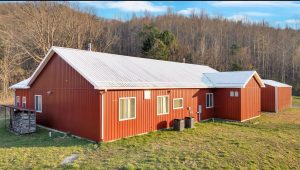back and side view of a red modern farmhouse shows multiple large windows and two heat pumps set discreetly at the side
