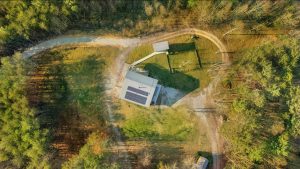 Overhead shot of large clearing with circular driveway around a house, a huge fenced dog play area and a fancy shed linked to the house by a walkway