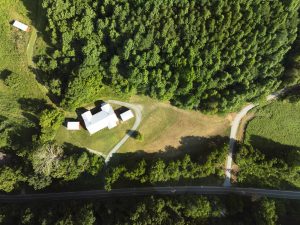 direct overhead shot of a sprawling white roof of a house and outbuildings in a field surrounded by trees