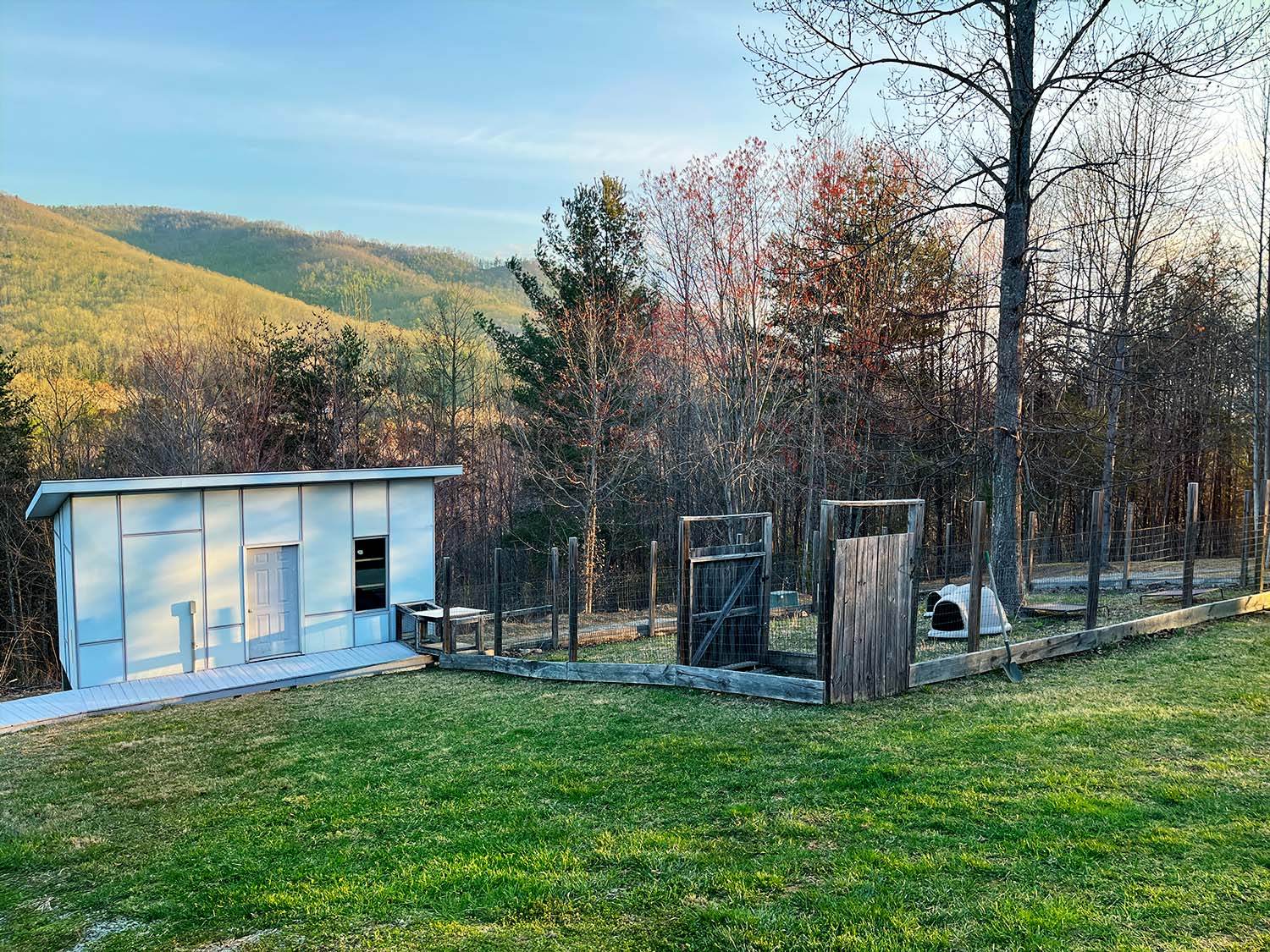 early morning light shines on the side of a mountain with a fancy blue shed in the foreground