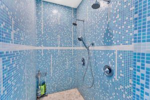 a vivid blue tiled shower with double rainfall shower heads and pebble tiled floor
