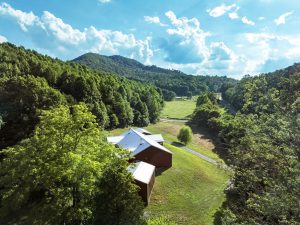 beautifully lit mountain valley with green fields and a red modern farmhouse with a white roof
