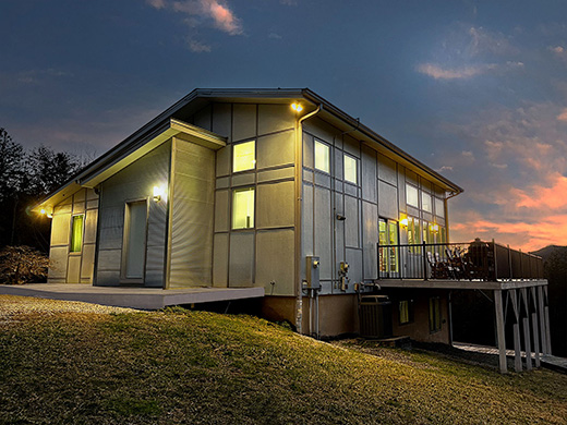 twilight photo of an angular contemporary house with a large deck facing a dramatic sunset