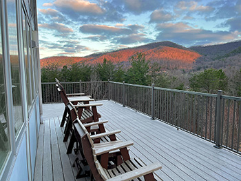 row of adirondack chairs on a deck faces an early morning sunrise reflecting off the mountain ranges