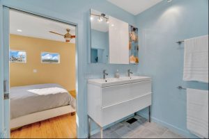 Ensuite bathroom has soothing blue walls and a glossy white vanity and a shelf with artwork