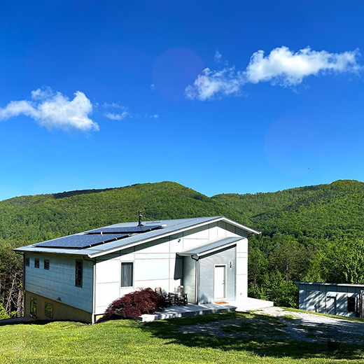 bright blue sky in the mountains with a light colored modern house dappled in sunlight