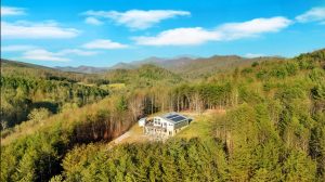 Stunning view of blue ridge mountains in the distance on a bright day with a contemporary house perched in a clearing on a ridgetop