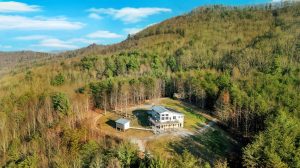 a grand contemporary home sits squarely in the center of a large grassy lawn surrounded by forested mountains