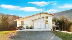 a bright photograph of the front of a contemporary styled home with a deck on the right side and a front porch that spans the entire front of the house
