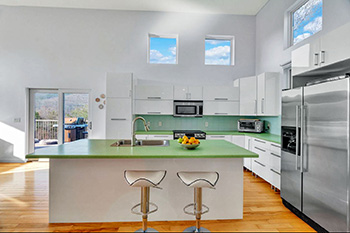large kitchen island with barstools faces a giant glass patio door open to mountain views