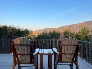 two adirondack chairs face the mountains as the sunrise makes the leaves glow