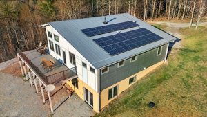 Closeup overhead of contemporary house with a metal roof, solar panels and large deck with dining table set up for 6