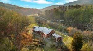 a pastoral overhead photo of a modern red farmhouse with multiple porches, several outbuildings, and a circular driveway that leads to the pasture