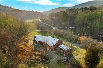 postcard perfect aerial photo of a long mountain valley with a large red barndominium nestled on a hilltop