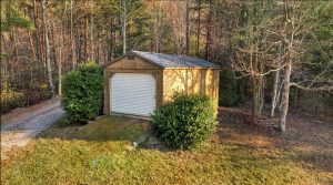 rustic tractor shed with white garage door sits in an alley of trees and shrubs