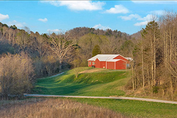 early sunset view of a red-sided modern farmhouse perched on a grassy knoll