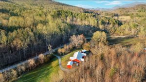 Overhead photograph showing mountain ridges, trees and a sprawling modern farmhouse complex with red siding and a white roof
