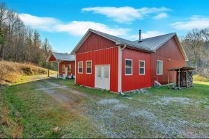 Side-front view of a red metal modern farmhouse with a stack of logs in a log rack