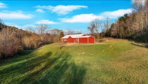 a modern red barndominium stands on top of a hill at the edge of a green grassy field